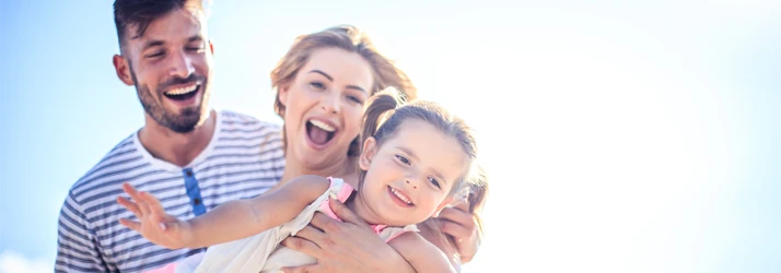 Two adults and one child positioned closely together against a bright sky background, with faces oriented toward the camera.