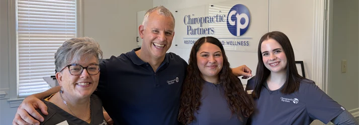 Dr. Alan Houfek and staff members standing together indoors in front of a wall sign reading “Chiropractic Partners,” posing closely side by side.